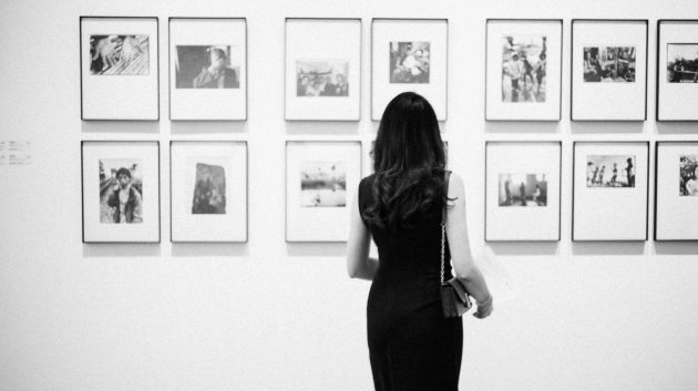 grayscale photo of woman watching photos on wall